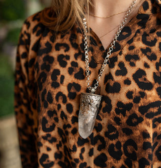 Model in leopard print top wears a large crystal point pendant in a silver setting on silver chain
