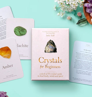 Box and sample Amber and Malachite cards from the Crystals for Beginners deck rest on an aqua surface scattered with crystals and flowers