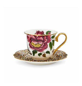 White floral teacup with gold rim and handle rests in the center of a leopard print saucer with scalloped, gold-painted rim
