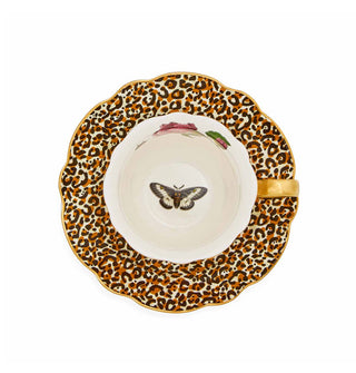 Top view of a gold-handled teacup with moth design in its bottom atop a leopard print saucer with gold scalloped edge