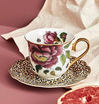 Floral teacup and leopard print saucer, both with gold accents, on a pink surface with crinkled paper and halved grapefruit