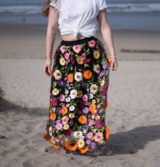 Model wears a black skirt embroidered with colorful, all-over three-dimensional flowers on a sunny beach