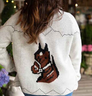 Model wears a long-sleeved white cardigan with diamond and zigzag detail designs and a brown bridled horse head graphic on the back