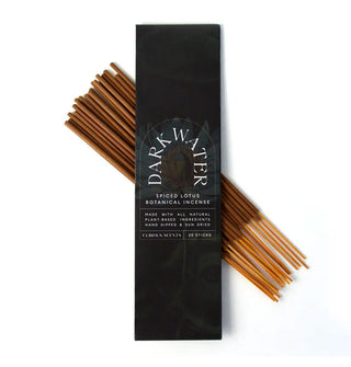 Darkly illustrated rectangular pack of Dark Water Spiced Lotus Botanical Incense is placed atop a bundle of 20 sticks