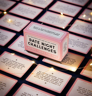 Date Night Challenges game box rests atop sample cards from the deck illuminated by string lights