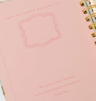 Notebook cover's pink interior says, "This notebook belongs to:" with a place to write your name, and toward the bottom is a quote by Anaïs Nin: "We write to taste life twice, in the moment and in retrospection."