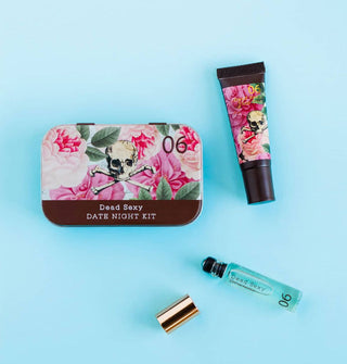 Mini perfume rollerball vial, lip gloss tube, and Dead Sexy Date Night Kit tin featuring lush floral patterning and skull and crossbones insignia