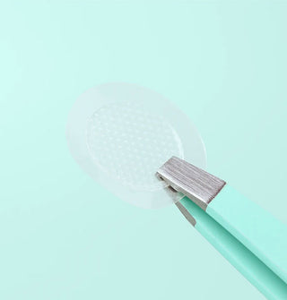 Closeup of a clear, round skin patch held with steel tweezer tips
