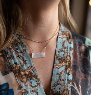 Model in patterned robe wears a selenite stone on gold chain around neck