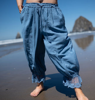 Model standing along the shoreline with sea stacks in the distance wears a pair of sky-blue, lace-trimmed pantaloons