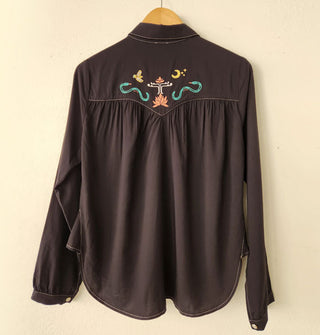 Back of a black Western-style shirt with colorful embroidered details on the yoke, gathering at the yoke seam, white stitching, and pearl snap buttons on the cuffs