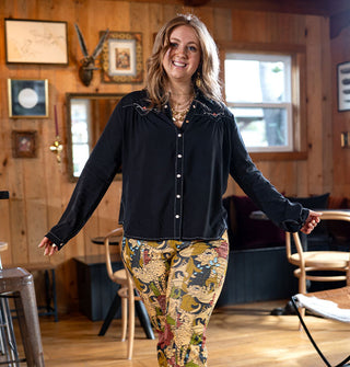 Smiling model with arms outstretched wears a lack Western-style snap button-front shirt with yoke and collar embroidery paired with a pair of densely patterned pants