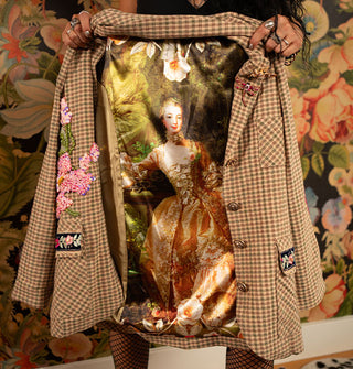 Model holds open a brown and green plaid blazer to reveal the Portrait of Madame de Pompadour by François Boucher on satin lining the inside