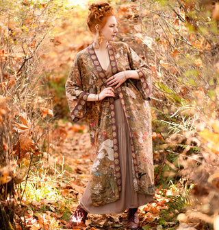 Model standing in an autumnal forest wears a long robe with an art nouveau print and contrasting border