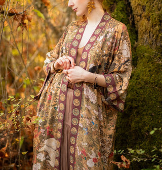 Model standing in an autumnal forest wears a long robe with an art nouveau print and contrasting border