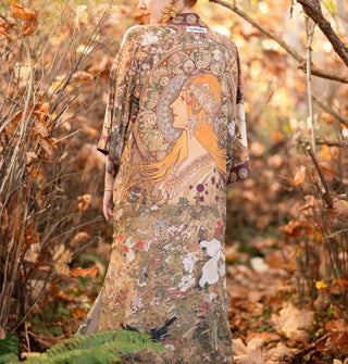 Model standing in an autumnal forest wears a long robe with an art nouveau print and contrasting border