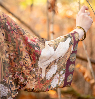 Model's arm wears the sleeve of a robe with an art nouveau doves design and contrasting border