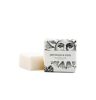Two 2-ounce bars of Driftwood & Soleil Shea Butter Soap, one wrapped in black and white sun print paper and the other unwrapped beside it