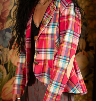 Model wears a pink and multicolored blazer with two mismatched button closures and two gold brooches on the lapel