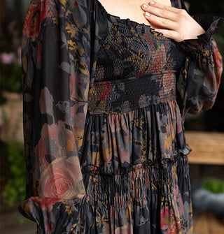 Model with hand to chest wears a dark rose print smocked dress with ruffled details and a squared sweetheart neckline