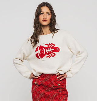 Model with hands on hips wears a white sweater with bright red embroidered lobster design on the front