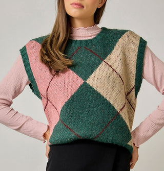 Model with hands on hips wears a green, beige, pink, and burgundy argyle sweater vest with cap sleeves and ribbed hems over a pink lettuce-edged mock turtleneck