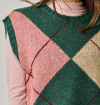 Model wears a green, beige, pink, and burgundy argyle sweater vest with cap sleeves and ribbed hems over a pink lettuce-edged mock turtleneck