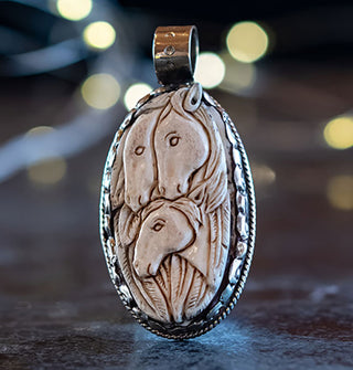 Oval pendant features carved bone image of three horses surrounded by feathers in a silver setting with rounded top bail