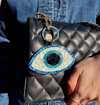 Model holds a quilted black clutch with blue and white evil eye keychain attached