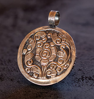 Silver pendant back side features ornate floral engraving