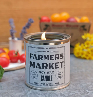 Lit Farmers Market Soy Wax Candle rests on a tabletop decorated with fresh flowers and tomatoes