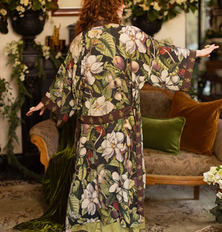 Model with arms outstretched wears a long robe with large, lush floral pattern and brown trim and belt with gold bees pattern