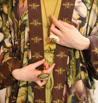 Model wears a long robe with large, lush floral pattern and brown trim with gold bees