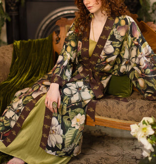 Model wears a long robe with large, lush floral pattern and brown trim with gold bees