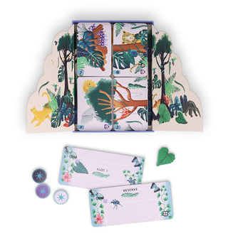 Some cards and pieces belonging to the Flora & Fauna rainforest game are shown with the box which features fold-out scalloped-edge flaps illustrated with colorful rainforest plants and animals