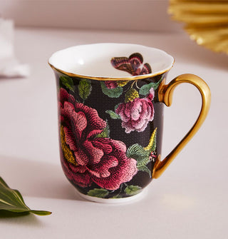 Black mug with lush floral pattern and white interior with butterfly graphic features gold rim and handle details