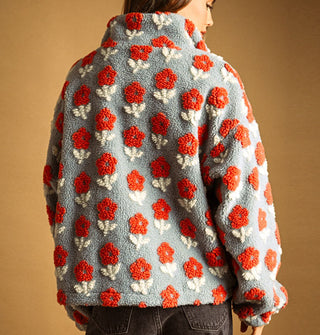 Model with back to camera wears a light blue sherpa jacket featuring all-over flocked orange and white flowers and a high collar