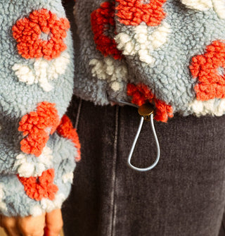 Closeup of the bottom drawstring toggle on a blue, orange, and white flower print sherpa jacket