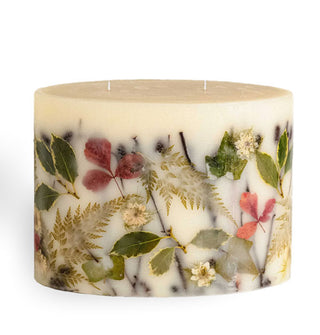 Large candle with two wicks features various leaves, ferns, and flowers embedded in its wax
