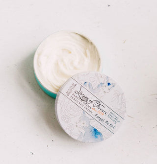 Opened round container of Library of Flowers Forget Me Not Parfum Crema with delicate, monochromatic illustrations of foxes and flowers reveals white, creamy product inside