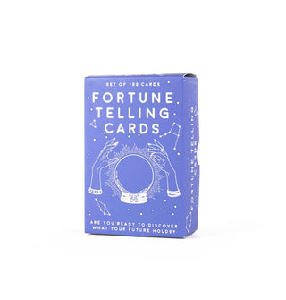 Periwinkle box of 100 Fortune Telling Cards features a central illustration of two hands positioned on either side of a crystal ball and surrounded by constellations
