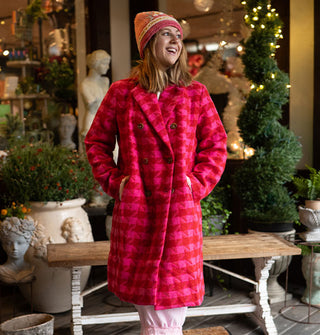 Smiling model wears a double-breasted pink and red houndstooth coat with a pink and white striped knit beanie