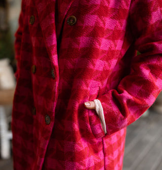 Model poses with hand in the pocket of a double-breasted pink and red houndstooth coat