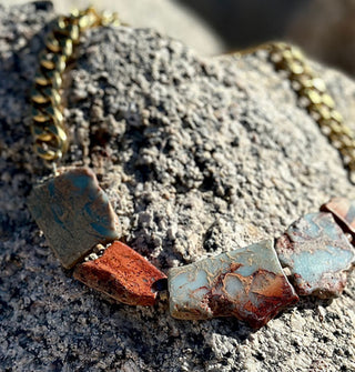 Necklace made of natural jasper stones strung on thick gold-toned curb chain rests on a porous rock