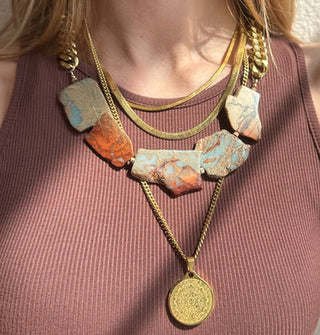 Model wears a necklace made of natural jasper stones strung on thick gold-toned curb chain with other gold necklaces