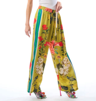 Model wears wide-legged chartreuse pants with a large floral print, side seam contrast stripes, and an elastic waistband with ties