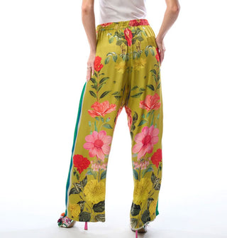 Model wears wide-legged chartreuse pants with a large floral print, side seam contrast stripes, and an elastic waistband