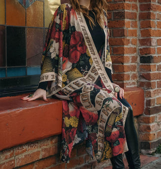 Model sitting on the ledge of a stained glass window wears a colorful printed robe with trim that says, "Friendship, love and truth" in wood-effect lettering