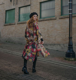 Model wearing a slightly billowing colorful printed robe walks away from the camera, looking back