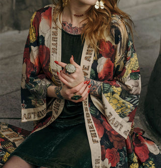 Seated model with hands clasped wears a colorful printed robe with the words, "Friendship, love and truth" on its trim in wood-like lettering